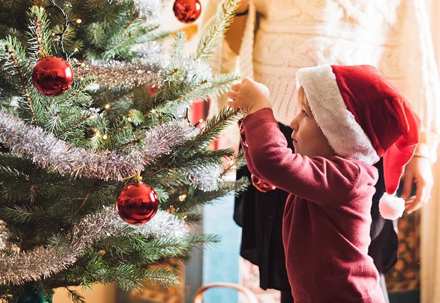 Pieni poika tonttuhattu päässään koristelemassa joulukuusta.